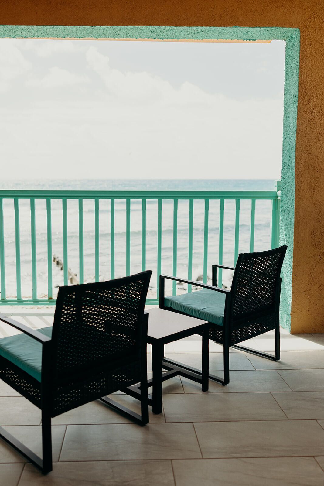A balcony with two chairs and a table, overlooking the sea.