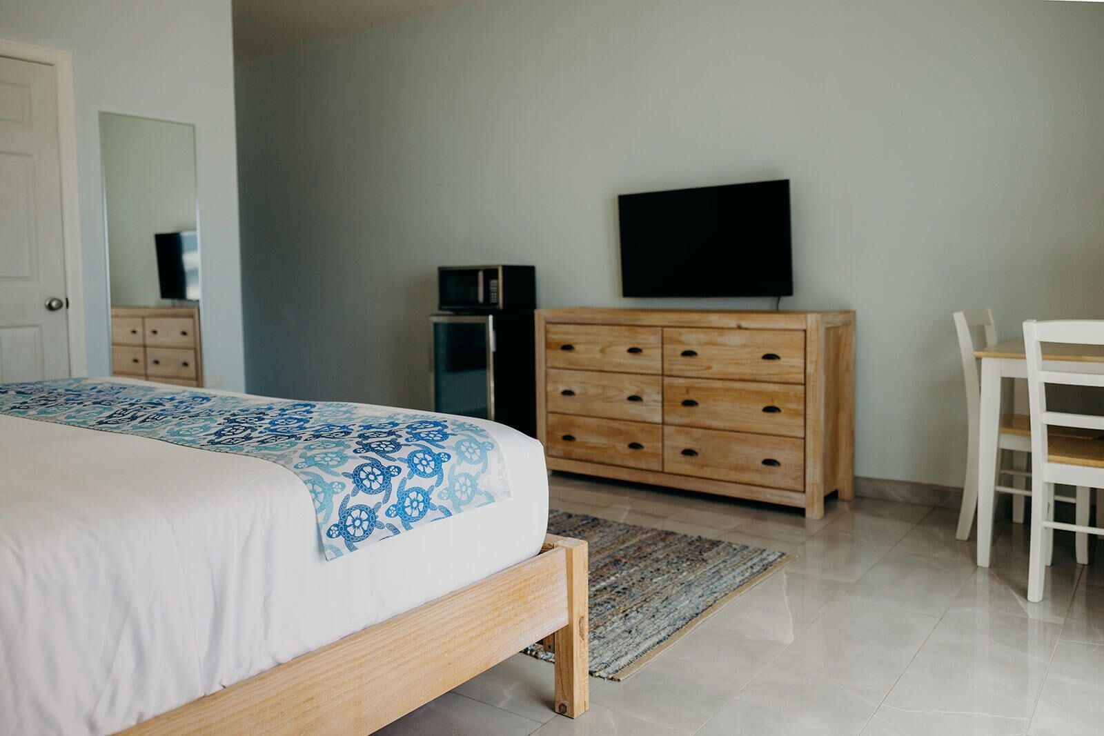 A bedroom with a bed, wooden dresser, TV, and a chair.