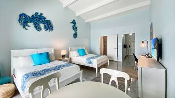 Habitación de hotel con dos camas, un escritorio, una silla y un televisor. Se observan obras de arte decorativas en las paredes y una puerta que da a otra habitación.