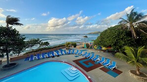 Un área de piscina con sillas reclinables azules, una piscina y vistas al océano.