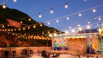 An outdoor patio with string lights, a mural, and stone walls.