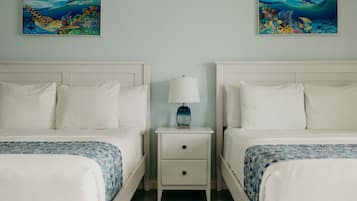 A hotel room with two beds, a nightstand with a lamp, and two wall-mounted paintings of underwater scenes.