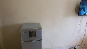 A small, grey refrigerator with a visible brand label, a wall-mounted television, and a power outlet on the floor. - BEDROOM DAKAR PLATEAU (Dakar)