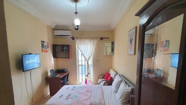 A hotel room with a bed, bedside table, TV, desk, and an air conditioning unit. - BEDROOM DAKAR PLATEAU (Dakar)