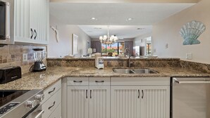 Una cocina con encimeras de granito, armarios blancos, horno empotrado y lavavajillas.