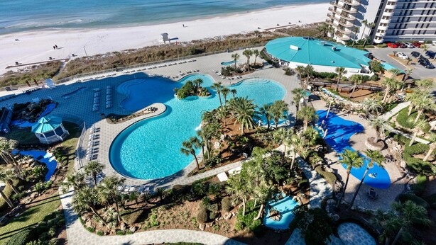 Un resort con varias piscinas, una playa y edificios altos al fondo.