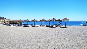 Une plage avec des chaises longues et des parasols en chaume.