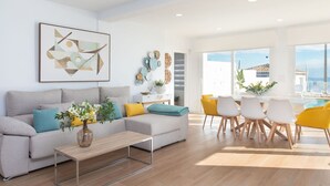 Un salon moderne avec un canapé, une table basse et des fauteuils jaunes. Une grande fenêtre offre une vue sur la mer.