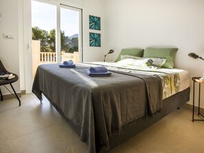 A bedroom with a bed, a chair, a desk, and a balcony.
