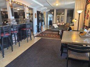 Moderni keittiö, jossa on baaritiski, ruokapöytä tuoleineen, kuviollinen matto sekä viihtyisä oleskelutila, jossa on sohva ja koriste-esineitä.