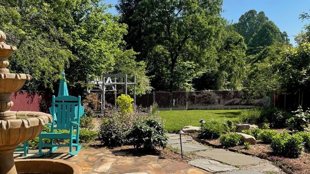 A stone patio with a fountain, a blue chair, and a playground structure. - Sunset Cottage Blocks from Downtown (Brevard)