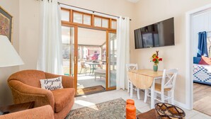 A cozy living area with a sofa, a coffee table, a TV mounted on the wall, and a sliding glass door leading to an outdoor patio. - Sunset Cottage Blocks from Downtown (Brevard)
