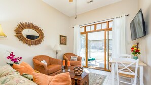 A living room with a sofa, two armchairs, a coffee table, a TV, and a sliding glass door leading to an outdoor area. - Sunset Cottage Blocks from Downtown (Brevard)