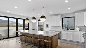 Uma cozinha moderna com uma ilha grande, banquetas, armários brancos e iluminação pendente.