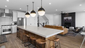 Uma cozinha moderna com ilha central, banquetas, eletrodomésticos de aço inoxidável e iluminação pendente.
