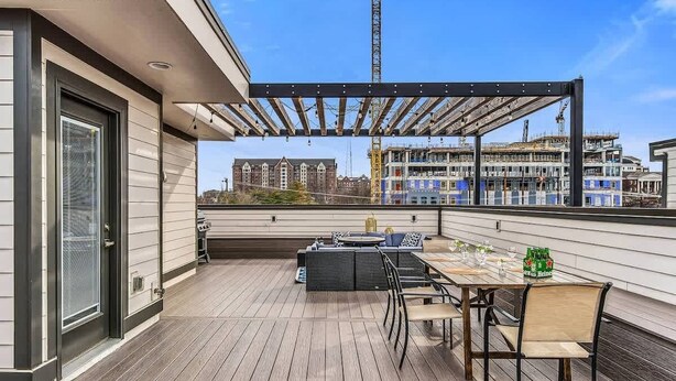 Una terraza en la azotea con una mesa y sillas, una parrilla y vistas a una obra en construcción de fondo.