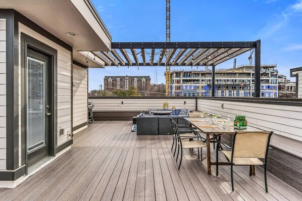 Una terraza en la azotea con una mesa y sillas, una parrilla y vistas a una obra en construcción de fondo.