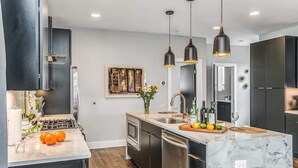 Una cocina moderna con armarios oscuros, una isla de mármol e iluminación colgante.