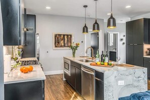 Una cocina moderna con armarios oscuros, una isla de mármol e iluminación colgante.