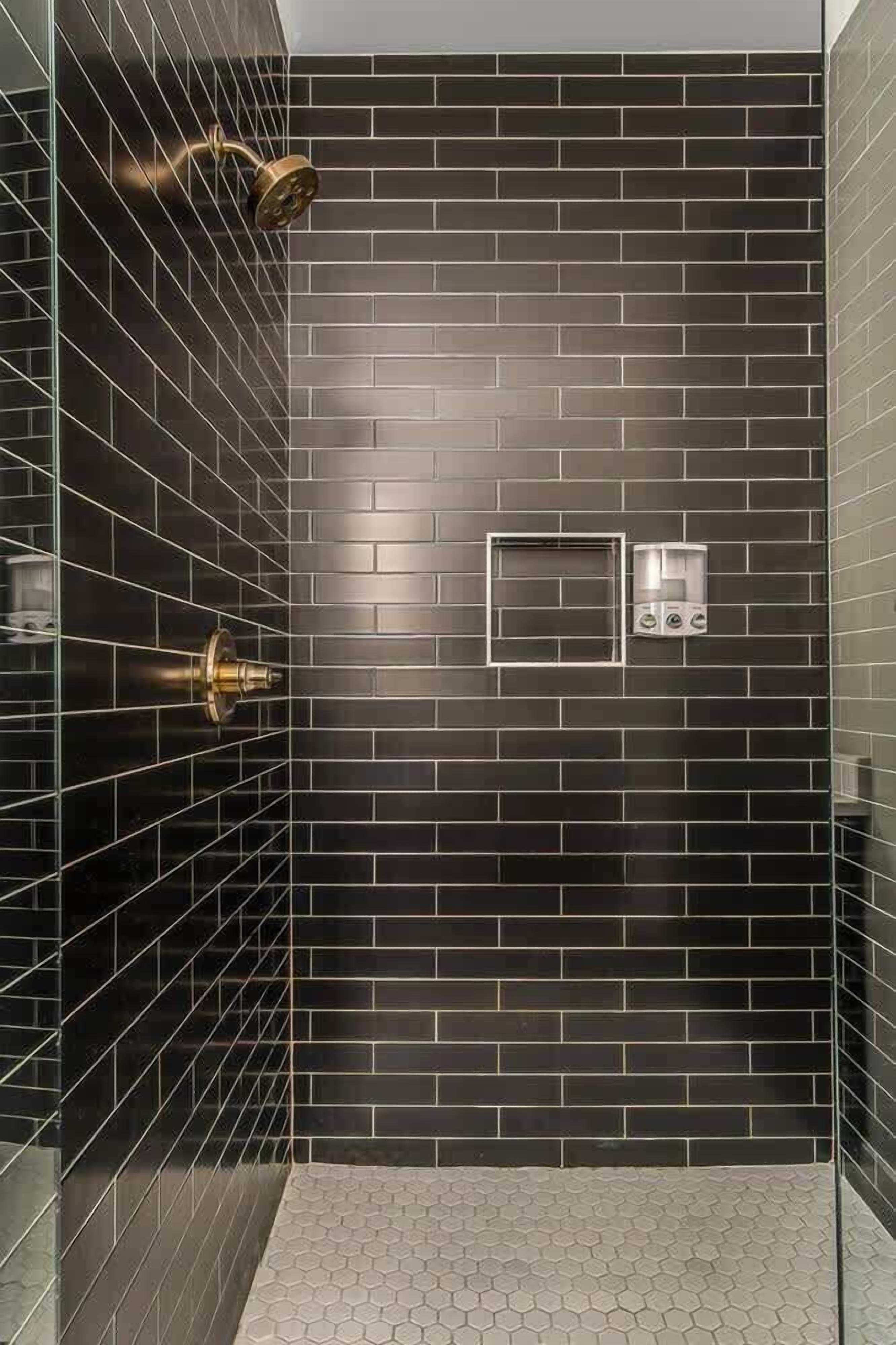 Une douche moderne avec des carreaux de couleur sombre, un espace clos en verre et un pommeau de douche à main.