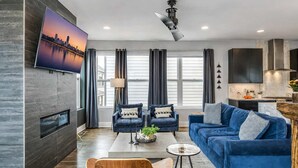 Una sala de estar moderna con un sofá azul, dos sillones, una mesa de centro y un televisor instalado en la pared.