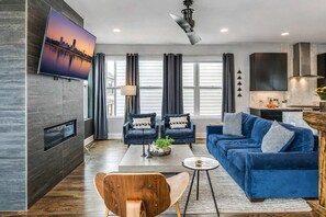 A modern living room with a blue sofa, two armchairs, a coffee table, and a TV mounted on a wall.