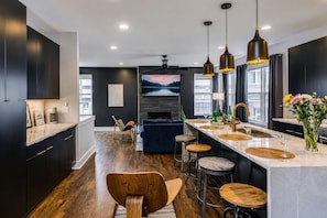 A modern kitchen with dark cabinetry, a central island with stools, a built-in TV, and a fireplace. - Nashville Escape - Gorgeous Home Near Broadway (Nashville)