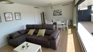 Una sala moderna con un sofá gris, una mesita blanca y un comedor con sillas blancas.