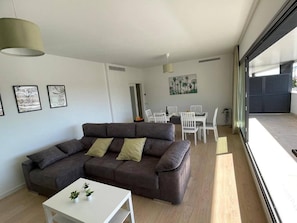 Una sala moderna con un sofá gris, una mesita blanca y un comedor con sillas blancas.