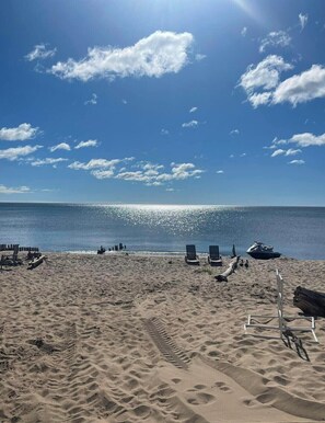 A beach with clear skies, a calm sea, and several lounge chairs and a jet ski on the sand. - Lake Huron Beach Front Cabin for two. (AuSable Twsp.)