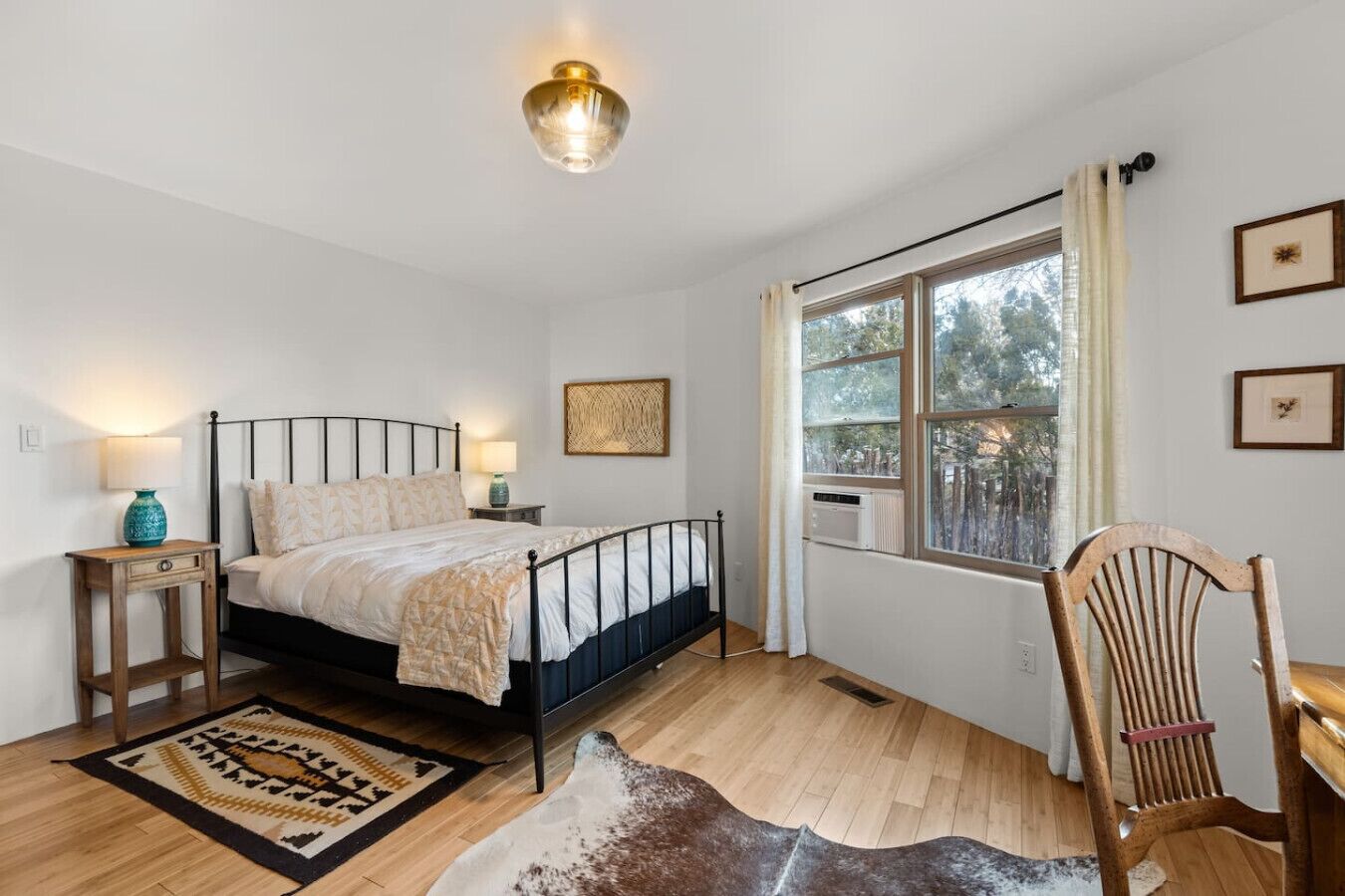 Une chambre à coucher avec un lit, une table de chevet, une chaise, une fenêtre et un luminaire au plafond.