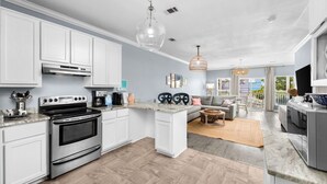 A modern kitchen with white cabinets, a stainless steel oven, and a dining area with a sofa and table. - FANTASTIC 2/2.5 TOWNHOME ON 30A!! SLEEPS 7!! WALKING DISTANCE TO GULF PLACE! (Santa Rosa Beach)