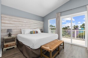 A bedroom with a bed, bench, nightstand, and a view of the outside.