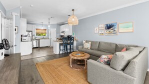 A modern living room with a grey sofa, a round coffee table, and a kitchen in the background. - FANTASTIC 2/2.5 TOWNHOME ON 30A!! SLEEPS 7!! WALKING DISTANCE TO GULF PLACE! (Santa Rosa Beach)