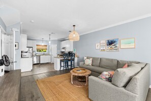A modern living room with a grey sofa, a round coffee table, and a kitchen in the background.