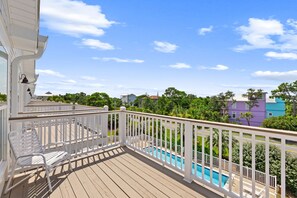 Terraza de madera con piscina, barandillas blancas y vistas a casas vecinas.