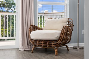 Una silla de mimbre con un cojín en una habitación con vista a la vegetación a través de una ventana.