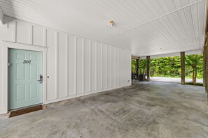 Un porche cubierto con piso de concreto, una puerta con el número 307, y vista a follaje exterior.