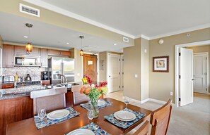 A modern kitchen with a central island, dining table set for four, and a living area with a door leading to another room.