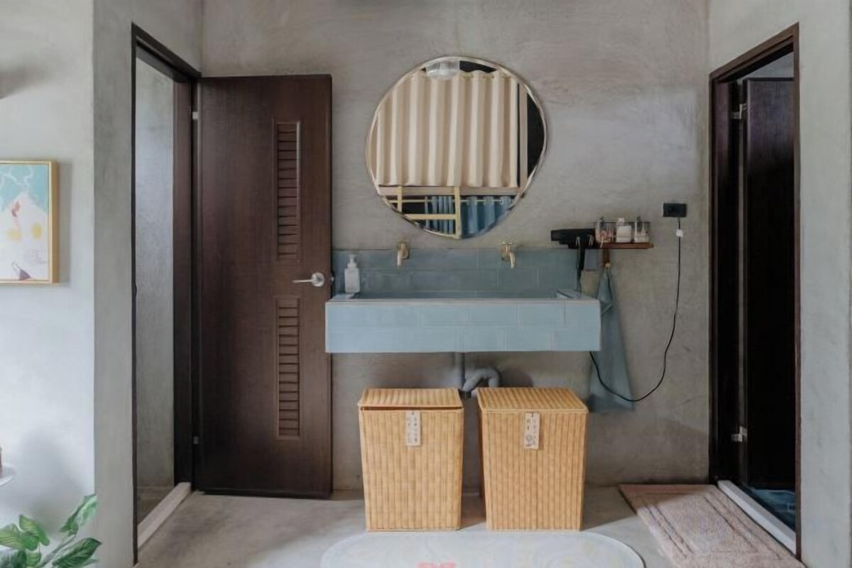 Un baño con un espejo redondo, un lavabo azul y dos cestas de mimbre.