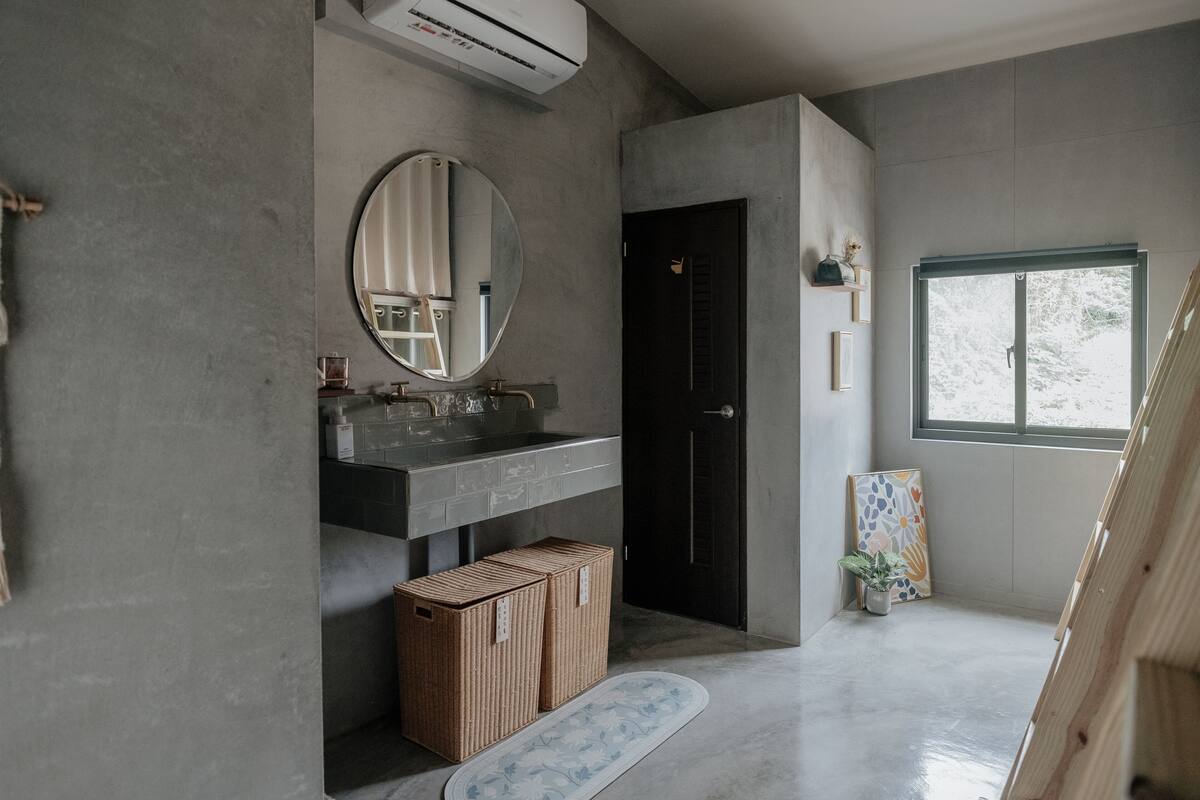 A modern bathroom with a large mirror, a black door, a window, and a wooden bench.