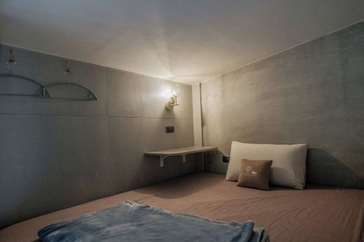 A bedroom with a bed, a nightstand, a wall-mounted light, and a hanging towel rack.
