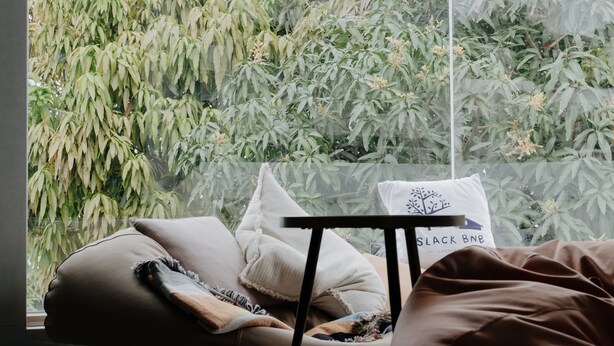 A modern room with a large window, a bed with pillows, a small table, and a hanging light fixture. - Slack BnB - Hostel (Liuqiu)