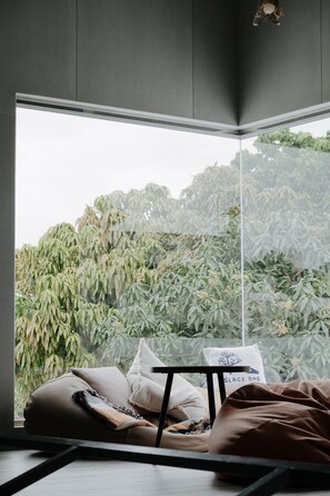 Een moderne kamer met een groot raam, een bed met kussens, een kleine tafel en een hanglamp.