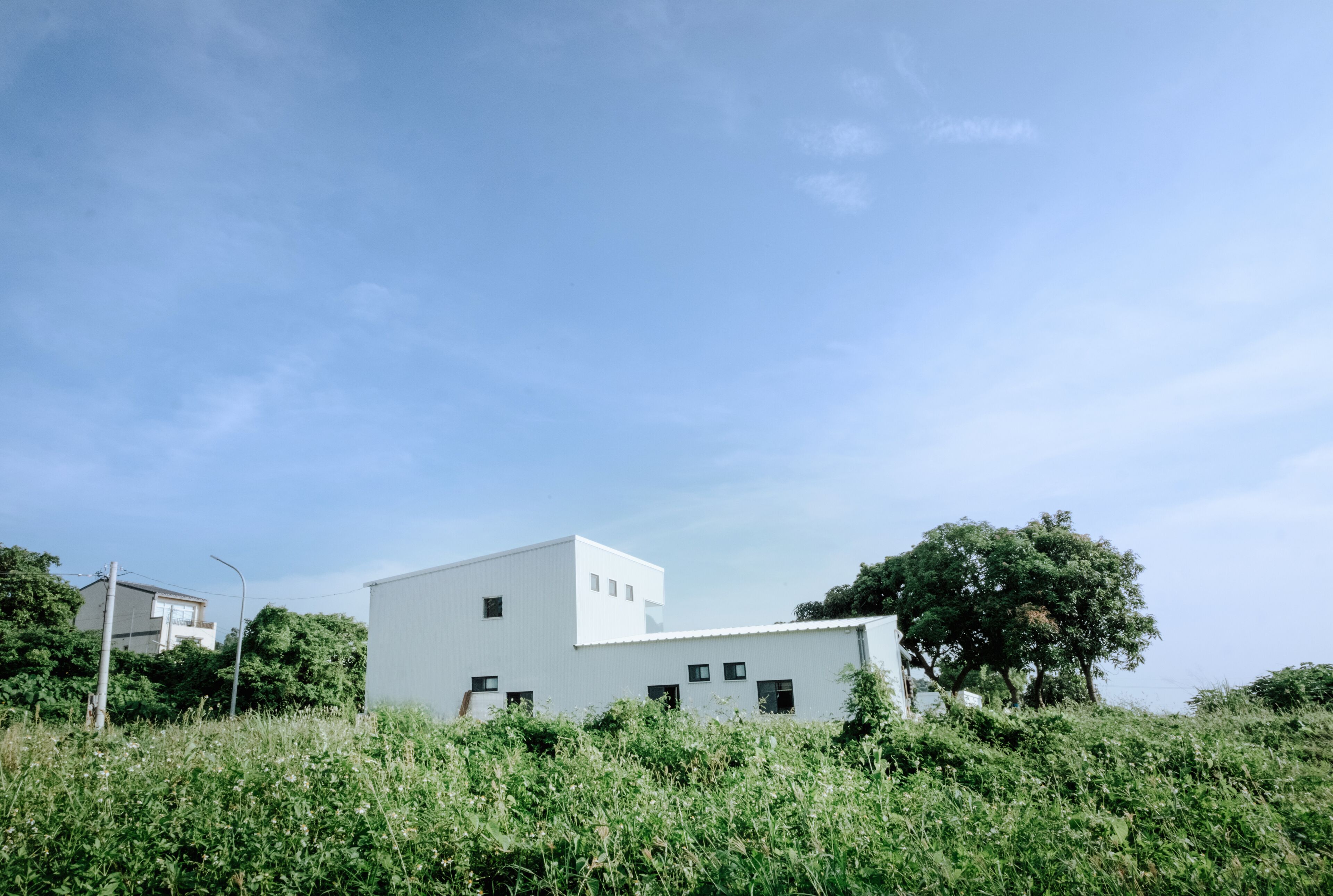 A modern white building with a flat roof, surrounded by lush greenery and a clear blue sky.
