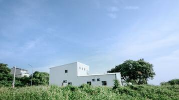 A modern white building with a flat roof, surrounded by lush greenery and a clear blue sky.