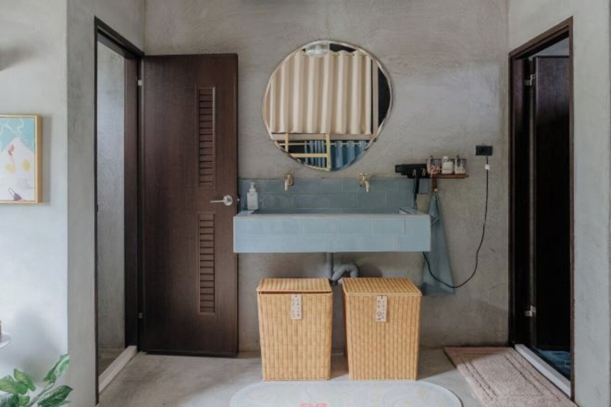 A bathroom with a wooden door, a round mirror, a blue sink, and two wicker baskets on the floor.