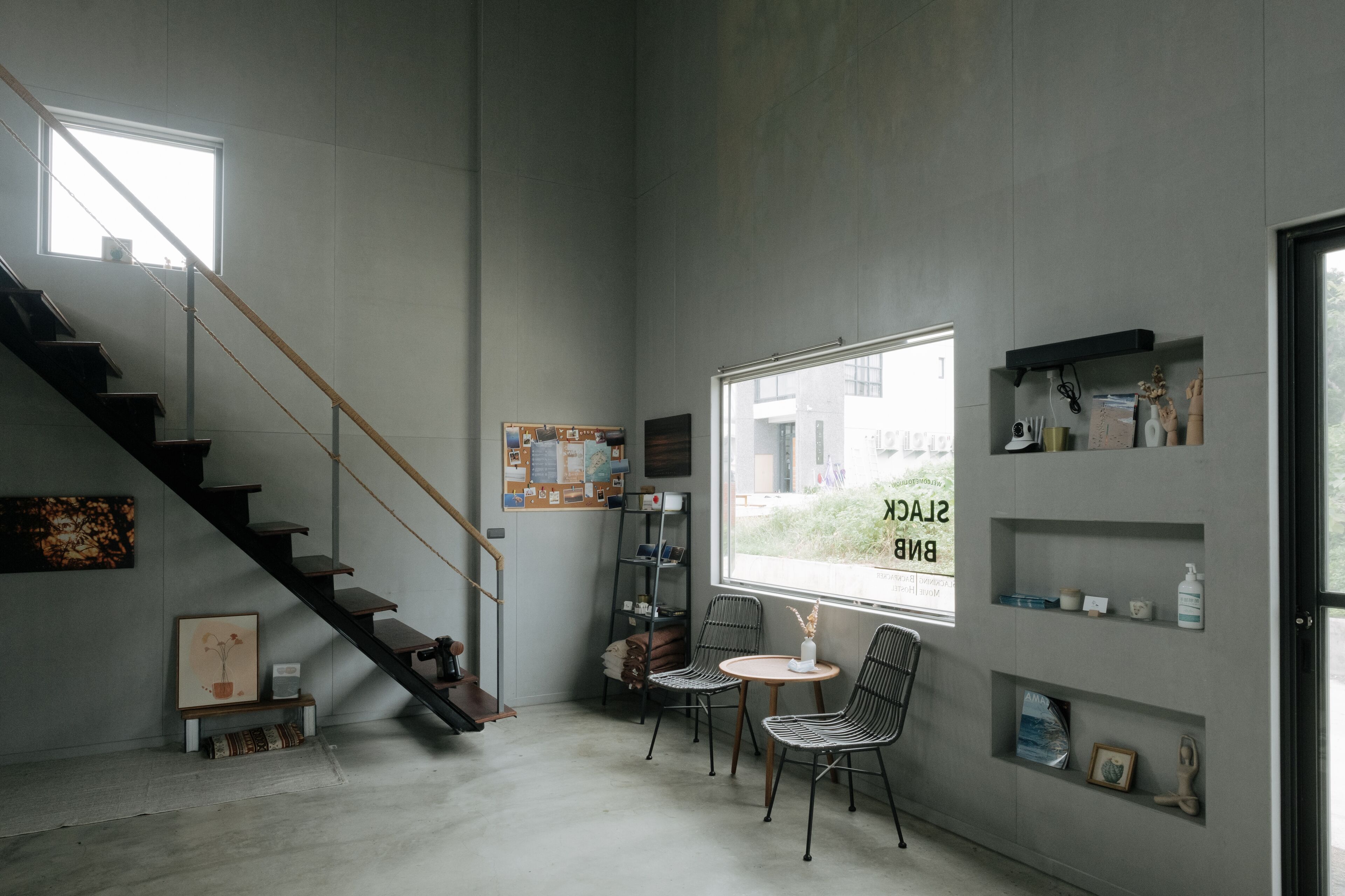 Un interior moderno con una escalera, un ventanal con vistas y una zona de estar con sillas y una mesita.