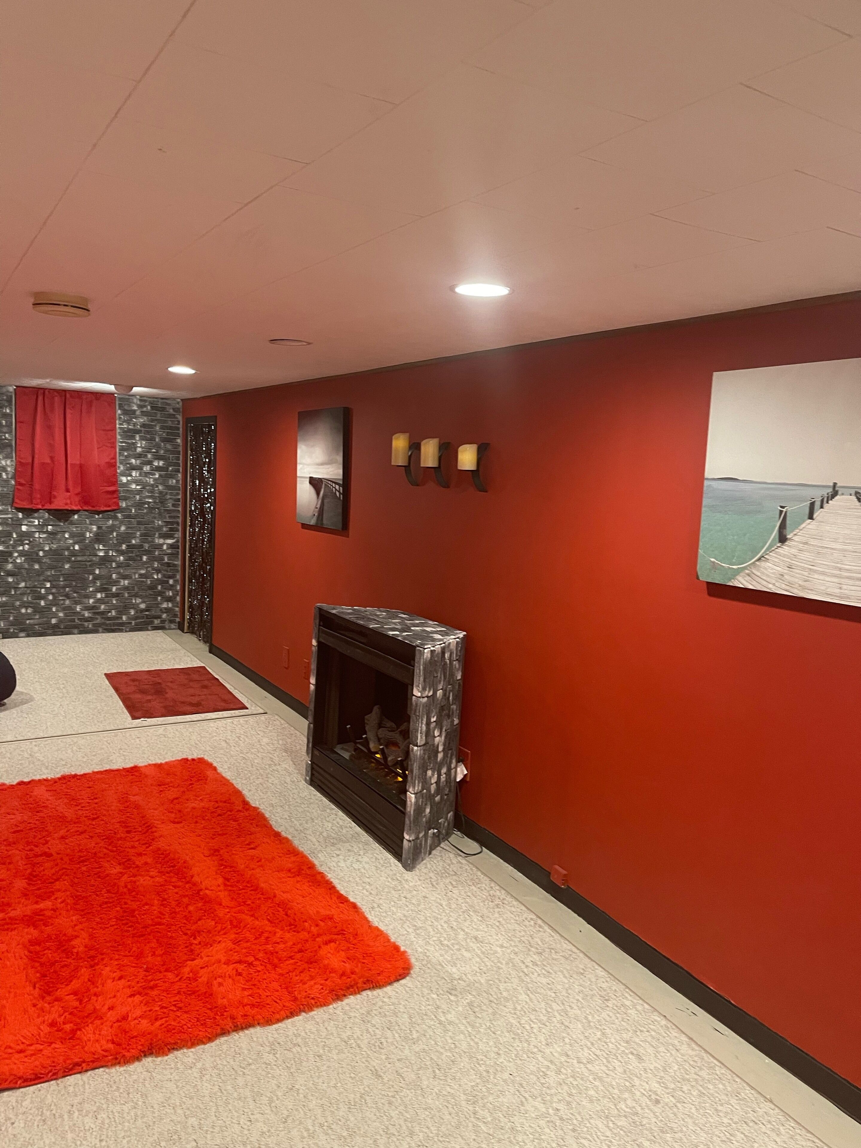Une pièce avec une cheminée, des murs rouges, une grande moquette rouge et un tableau représentant une jetée.