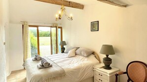 Un dormitorio con una cama grande, dos mesitas de noche con lámparas, una silla y vistas a un jardín a través de una ventana.